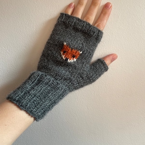 Könnte beinhalten: Graue Fingerlose Handschuhe mit einem gestrickten Fuchs-Design auf dem Handrücken.