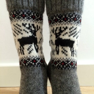 May include: A pair of grey wool socks with a white and black reindeer pattern. The socks have a red and black trim around the top.