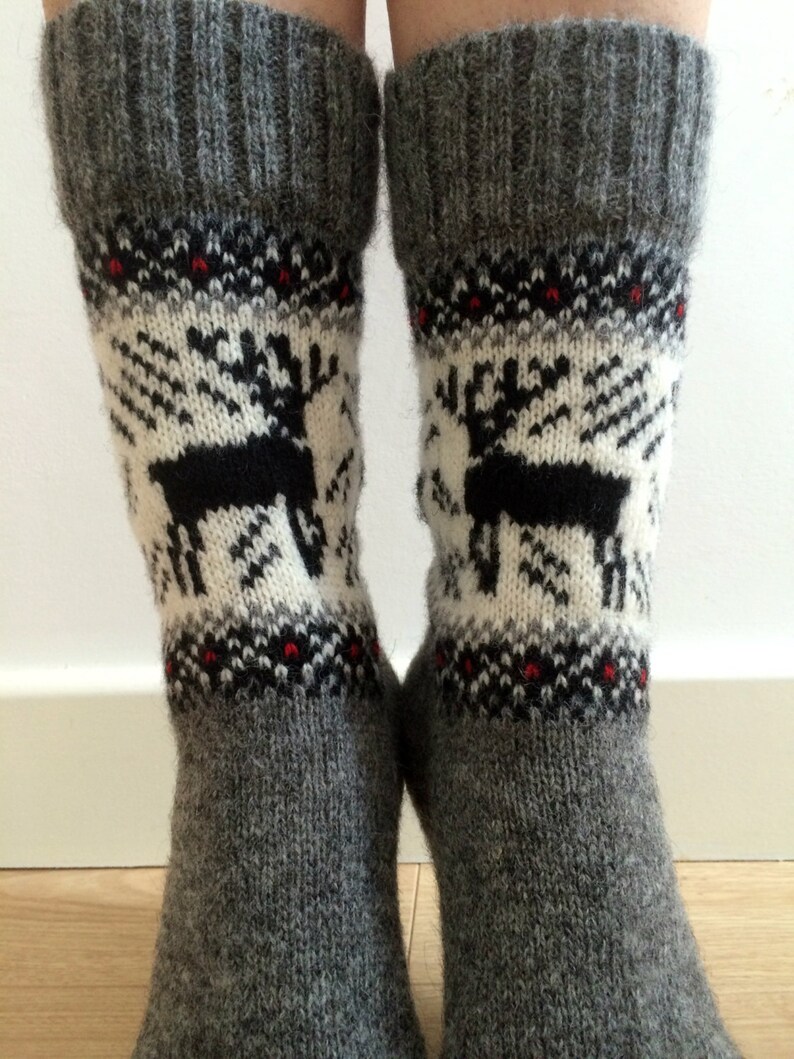 May include: A pair of grey wool socks with a white and black reindeer pattern. The socks have a red and black trim around the top.