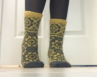 May include: A pair of knitted socks with a yellow and black geometric pattern. The socks are worn on a person's feet.