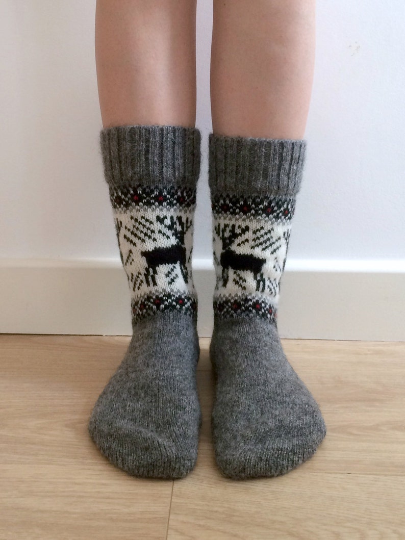 May include: Grey wool socks with a white and black reindeer pattern. The socks have a red and black trim around the top.