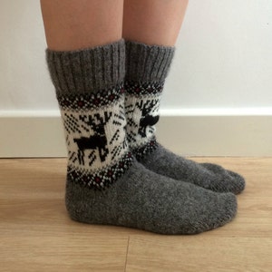 May include: A pair of grey wool socks with a white and black reindeer pattern. The socks are knitted and have a ribbed cuff.