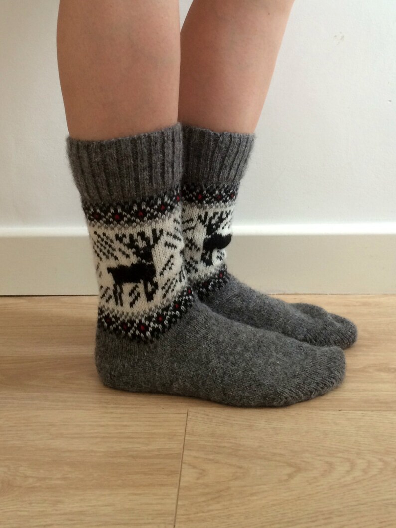 May include: A pair of grey wool socks with a white and black reindeer pattern. The socks are knitted and have a ribbed cuff.