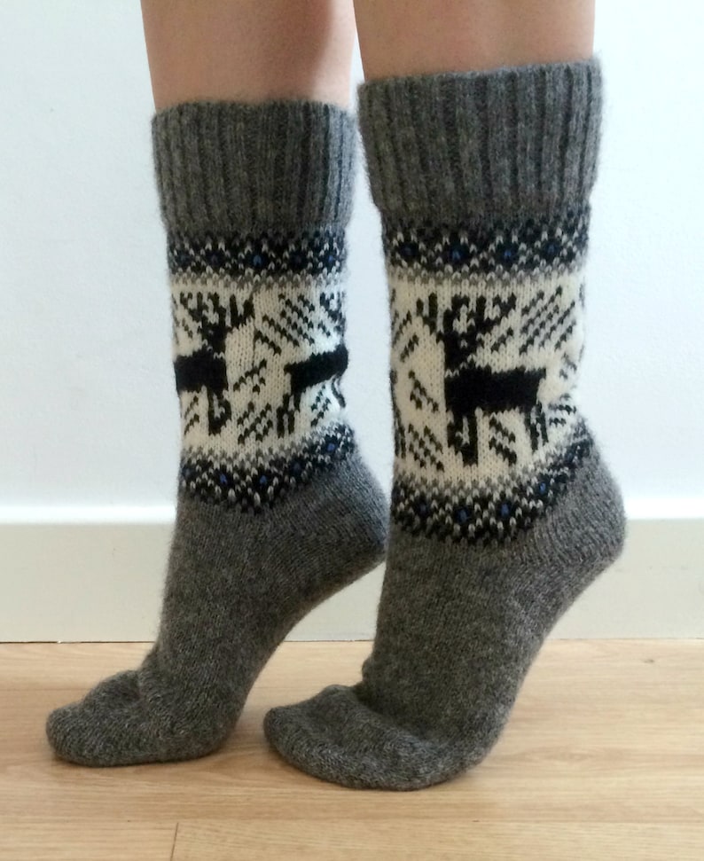 May include: A pair of gray wool socks with a white and black reindeer pattern. The socks have a blue and white geometric pattern around the top.
