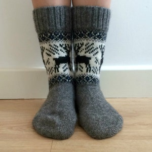 May include: A pair of gray wool socks with a white and black reindeer pattern. The socks are folded down at the top, revealing a blue and white stripe.