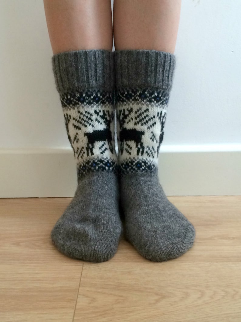 May include: A pair of gray wool socks with a white and black reindeer pattern. The socks are folded down at the top, revealing a blue and white stripe.