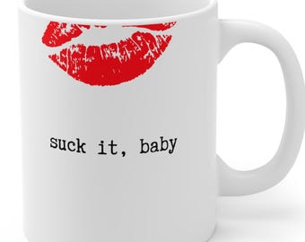 May include: White ceramic mug featuring a red lipstick kiss mark and the phrase "suck it, baby" in black text. The mug has a curved handle and a glossy finish, suitable for hot or cold beverages.