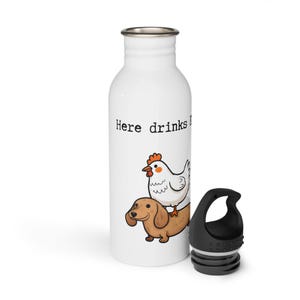Könnte beinhalten: Weiße Wasserflasche mit schwarzem Deckel. Die Flasche zeigt eine Cartoon-Illustration eines Huhns, das einen Dackel reitet, mit dem Text "Here drinks". Die Flasche ist für kalte Getränke konzipiert.