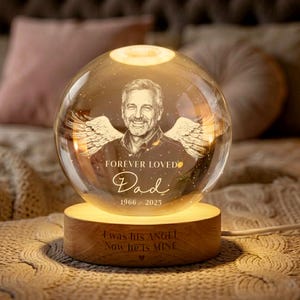 May include: A memorial sphere lamp with a portrait of a man, angel wings, and the text "Forever Loved Dad 1966-2025." The wooden base reads "I was his ANGEL Now he is MINE." The lamp emits a warm glow.