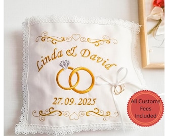 Peut inclure: Coussin de porteur d'anneaux blanc avec texte doré brodé "Linda & David" et la date "27.09.2025". Le coussin présente deux anneaux dorés et un diamant. Un ruban blanc est attaché.
