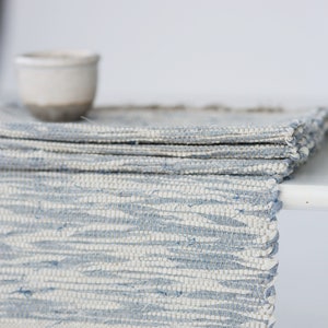 Könnte beinhalten: Ein gewebter Tischläufer in Blau und Weiß mit Fransen an den Enden. Der Läufer ist in der Mitte gefaltet und hat ein hellblaues und weißes Muster.