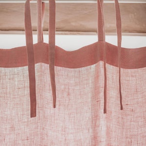 May include: A pair of pink linen curtains with a pink trim and tie-backs. The curtains are hanging from a white rod.