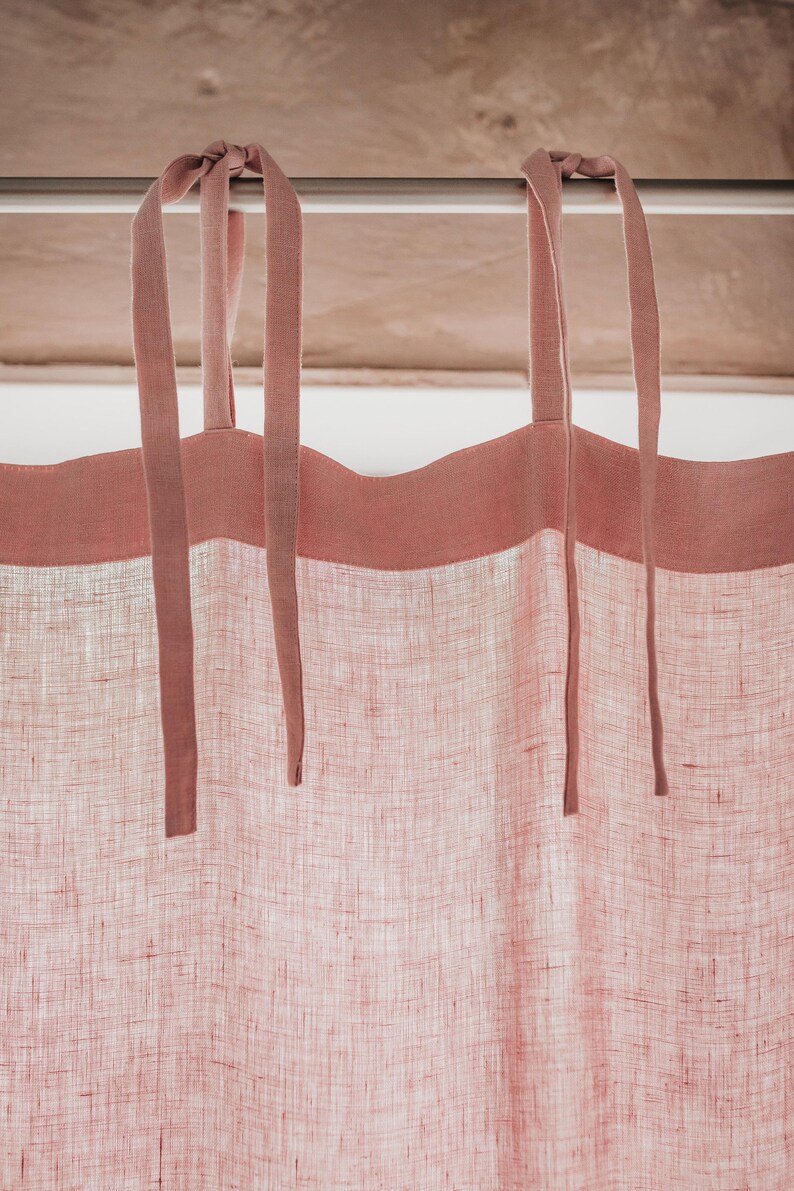 May include: A pair of pink linen curtains with a pink trim and tie-backs. The curtains are hanging from a white rod.
