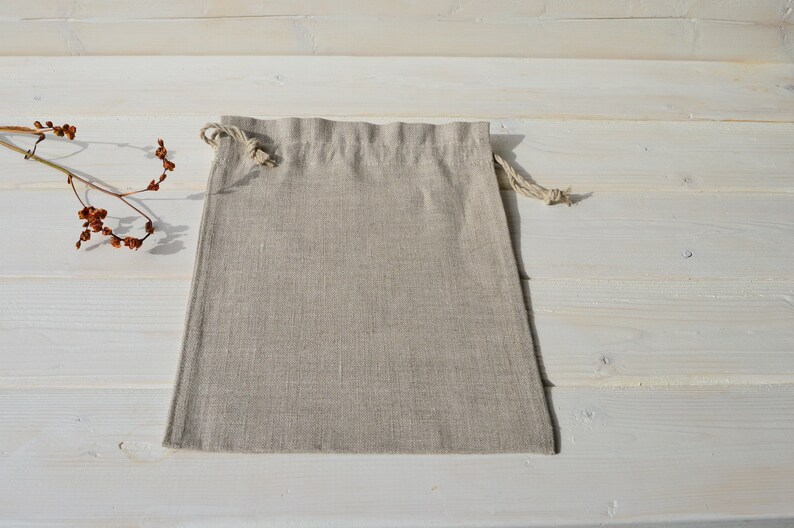 May include: A natural linen drawstring bag with a light beige color. The bag is empty and lying flat on a white wooden surface.