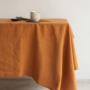 K&ouml;nnte beinhalten: Eine senfgelbe Tischdecke aus Leinen, die &uuml;ber einen Tisch gelegt ist. Die Tischdecke hat eine leicht zerknitterte Textur und h&auml;ngt an den Seiten des Tisches herunter.