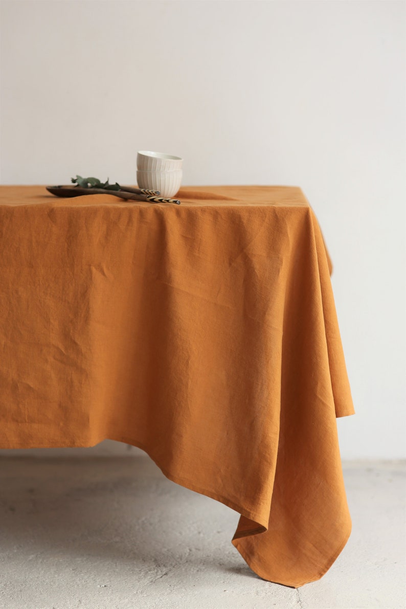 K&ouml;nnte beinhalten: Eine senfgelbe Tischdecke aus Leinen, die &uuml;ber einen Tisch gelegt ist. Die Tischdecke hat eine leicht zerknitterte Textur und h&auml;ngt an den Seiten des Tisches herunter.