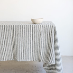 May include: A striped tablecloth in a neutral color palette, featuring vertical lines of dark gray and white. A small, speckled ceramic bowl sits on the table. The tablecloth drapes over the table's edge.