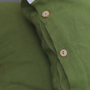Puede incluir: Dos fundas de almohada de lino verde con botones de madera. Las fundas de almohada tienen una etiqueta que dice "Linen Art".