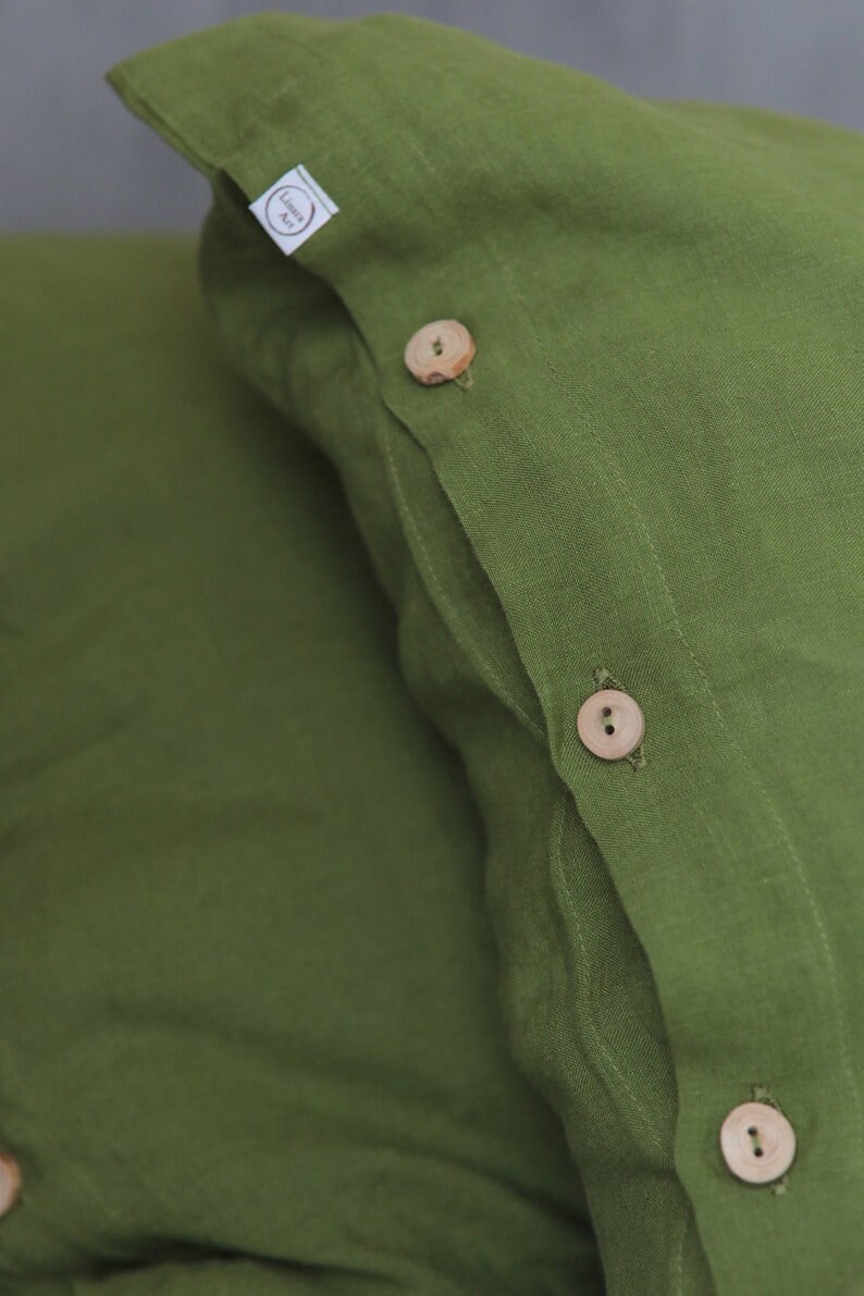 Puede incluir: Dos fundas de almohada de lino verde con botones de madera. Las fundas de almohada tienen una etiqueta que dice "Linen Art".
