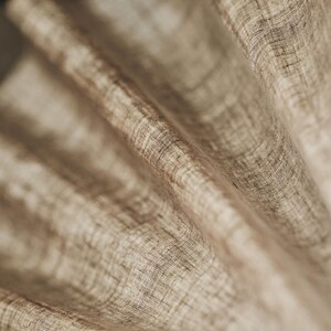 May include: Close-up of a beige fabric with a textured woven pattern. The fabric is folded and draped, creating soft folds and curves.