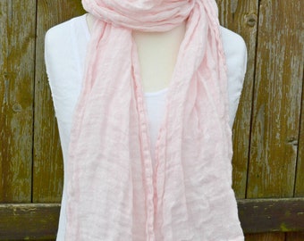 May include: A pale pink linen scarf draped over a white mannequin. The scarf is soft and crinkled, with a slightly frayed edge.