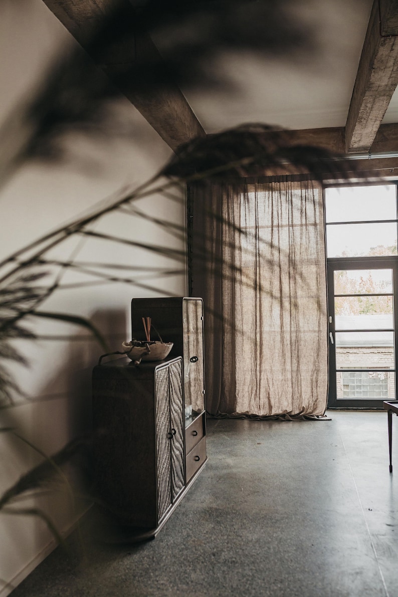 May include: A dark wood cabinet with a glass door and two drawers. The cabinet is in a room with a large window and a sheer curtain.