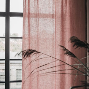 May include: A dusty rose linen curtain hangs in a window with a view of a brick building. The curtain has a simple design with ties at the top.
