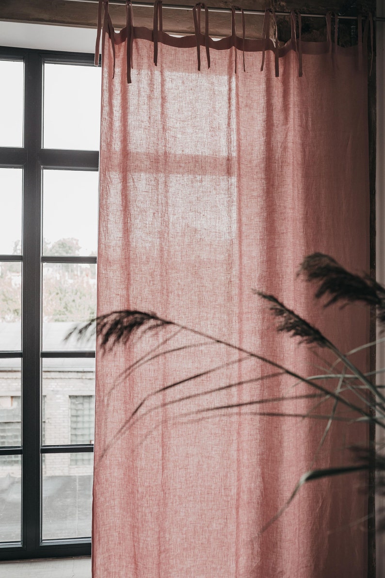 May include: A dusty rose linen curtain hangs in a window with a view of a brick building. The curtain has a simple design with ties at the top.