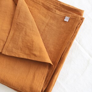 K&ouml;nnte beinhalten: Eine gefaltete, senfgelbe Tischdecke aus Leinen mit einem kleinen wei&szlig;en Etikett, auf dem "Linen & Love" in einem Kreis steht.