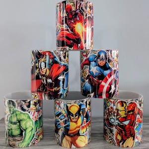May include: Six ceramic mugs featuring different comic book superhero designs. The mugs depict Deadpool, Thor, Captain America, Wolverine, Hulk and Iron Man. Each mug has a colourful comic book design with a different superhero.