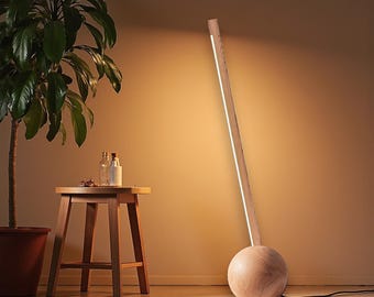 May include: A modern wooden floor lamp with a spherical base and a tall, slender, light-emitting column. The lamp has a natural wood finish and a bright, linear light source. The lamp is connected to a power outlet via a black cord.