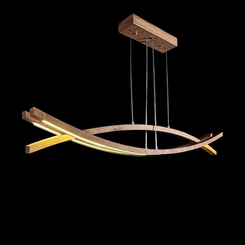 Puede incluir: L&aacute;mpara colgante moderna de madera con acabado natural. La l&aacute;mpara tiene una parte superior rectangular y dos vigas de madera curvas e intersecantes con iluminaci&oacute;n LED integrada. Cuelga de finos cables met&aacute;licos sobre un fondo negro. Mide aproximadamente 100 cm.
