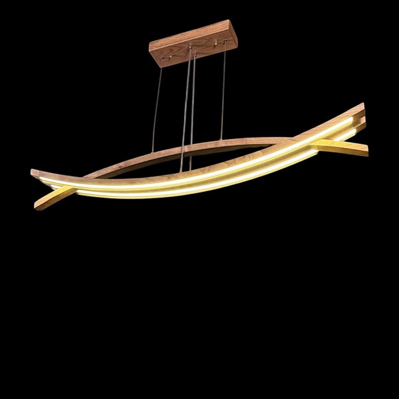 Puede incluir: Una moderna l&aacute;mpara colgante de madera con un dise&ntilde;o curvo en forma de barco. Cuenta con una marquesina rectangular de madera y est&aacute; suspendida por cables finos. La luz emite un brillo amarillo c&aacute;lido, creando un ambiente suave. El dise&ntilde;o es minimalista y elegante.