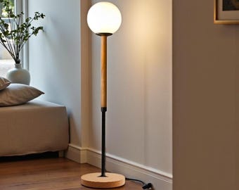 May include: A modern floor lamp with a spherical white glass shade. The lamp features a wooden pole, a black metal stem, and a round wooden base. The lamp is plugged into an electrical outlet and is positioned near a window.