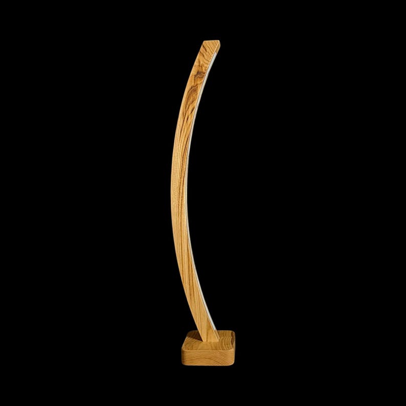 Op de afbeelding: Een gebogen houten sculptuur met een natuurlijke houtnerf afwerking. De sculptuur heeft een rechthoekige basis en een slanke, gebogen vorm. Het hout is lichtbruin en de achtergrond is zwart.