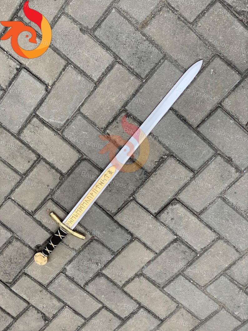 May include: A silver-bladed sword with a gold crossguard and a black-wrapped handle. The blade has gold lettering. The sword is lying on a gray brick surface. The sword is approximately 30 inches long.