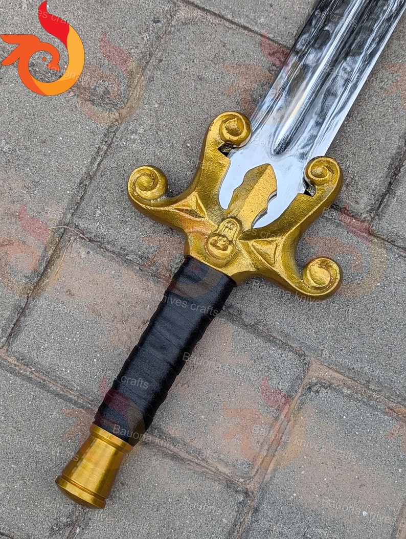 May include: A decorative sword with a polished silver blade and a gold-coloured hilt. The hilt features an ornate design with a black wrapped handle. The sword is likely a display piece or costume accessory.
