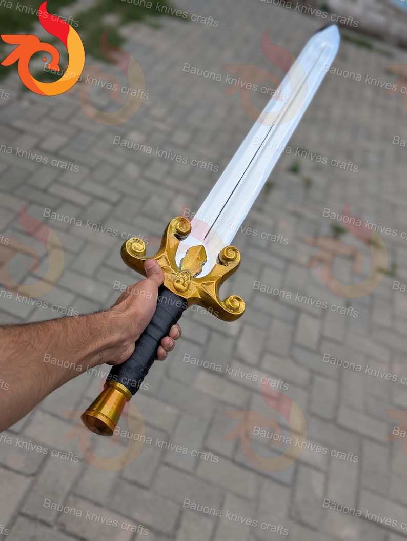 May include: A decorative sword with a silver blade and gold-coloured hilt. The hilt features ornate detailing and a black wrapped handle. The sword is held in a hand.