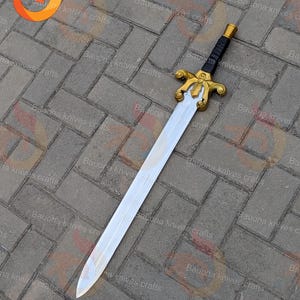 May include: A decorative sword with a silver blade and a gold-coloured hilt. The hilt features intricate designs and a black handle. The sword is displayed on a brick surface. The text "Bauona knives crafts" is visible.