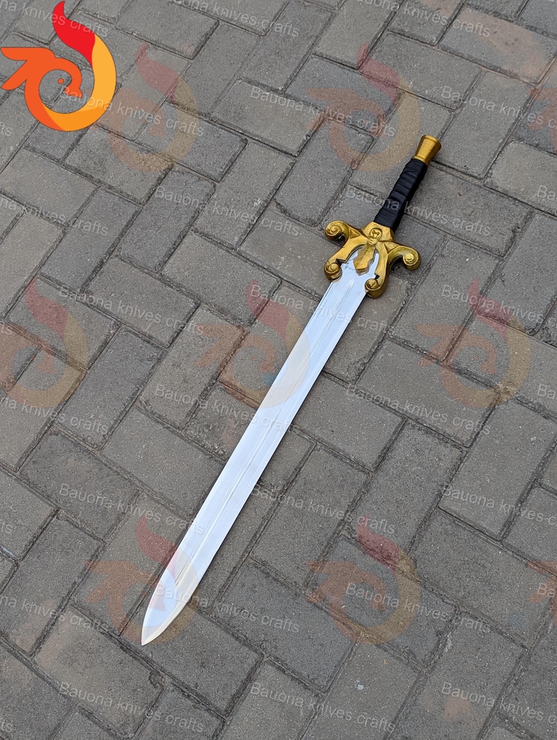 May include: A decorative sword with a silver blade and a gold-coloured hilt. The hilt features intricate designs and a black handle. The sword is displayed on a brick surface. The text "Bauona knives crafts" is visible.