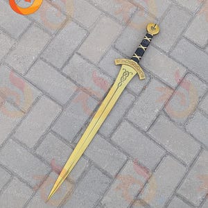 May include: A gold-colored sword featuring a double-edged blade with a central fuller. The crossguard and pommel are gold with intricate knotwork engravings. The handle is wrapped in black material with a gold crisscross pattern overlay.