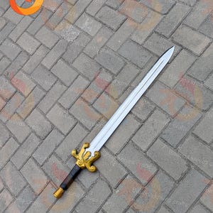 May include: A silver sword with a gold and black handle rests on a grey brick surface. The sword has a decorative gold hilt and a black grip. The blade is long and straight, with a sharp point.