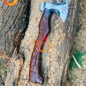 May include: A handcrafted axe with a dark brown wooden handle featuring intricate carvings. The axe head is silver with a dragon design. The axe is resting on a wooden surface with wood shavings.