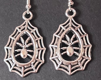 May include: A pair of silver-colored spiderweb earrings. Each earring features a teardrop-shaped design with a spiderweb frame and a spider in the center. The earrings have a hook closure.