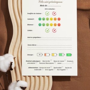 Peut inclure: Une feuille de papier blanche avec une liste de contrôle pour suivre les symptômes de la préménopause. La liste de contrôle comprend des sections pour les bouffées de chaleur, le sommeil, l'humeur, la libido, d'autres symptômes, des notes, les niveaux d'énergie, la douleur physique et l'alimentation. La liste de contrôle comprend des cases à cocher et une échelle de visages souriants pour évaluer la gravité des symptômes.