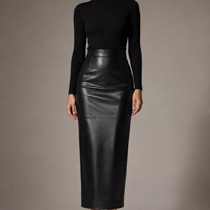 May include: A black long-sleeved mock neck top paired with a high-waisted black midi skirt made of a smooth, leather-like material. The skirt features a structured waistband, a clean silhouette, and a straight hemline that falls below the knees.