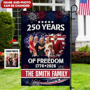 May include: A garden flag featuring a family photo, fireworks, and the text "250 YEARS OF FREEDOM 1776*2026 THE SMITH FAMILY" on a navy blue background. The flag is displayed on a metal stand in a garden.