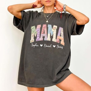 Op de afbeelding: Donkergrijs t-shirt met het woord "MAMA" in patchwork letters. De letters zijn in pastelkleuren en bloemmotieven. Daaronder staan de namen "Sophia", "Daniel" en "James" met hartjes.