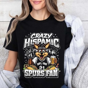 May include: Black t-shirt with a graphic that reads "Crazy Hispanic Spurs Fan." The graphic features a cartoon jackrabbit wearing a Spurs jersey, holding a beer and a foam finger. The shirt has a crew neck.