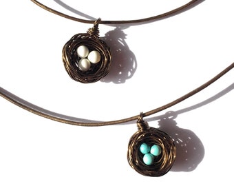 May include: Two necklaces with bird's nest pendants. One nest has three white beads, the other has three turquoise beads.